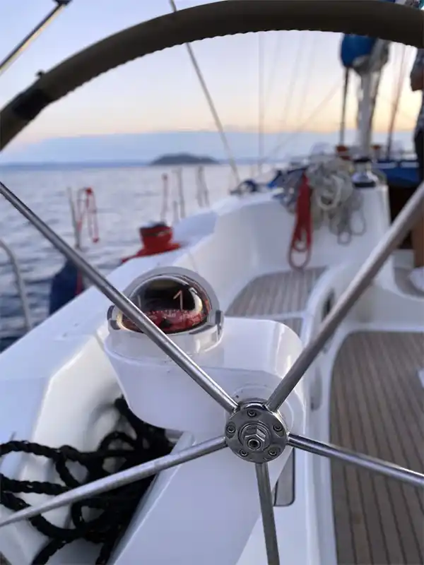 Steering wheel and cockpit of a sailing yacht at sea, an islet ahead