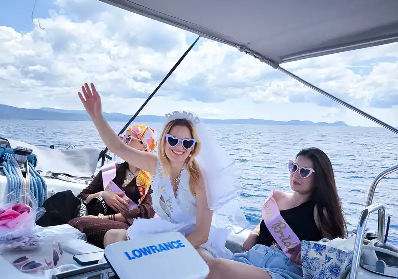 Bride-to-be and friends waving in the shaded cockpit of a sailing yacht