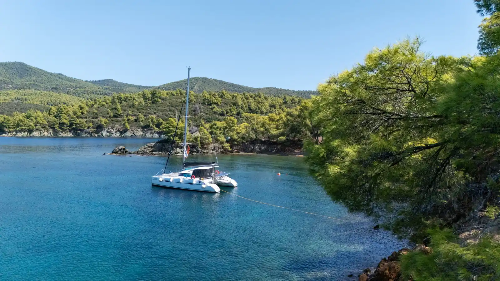 Catamaran anchored in a calm bay at Agia Kyriaki, framed by pine branches