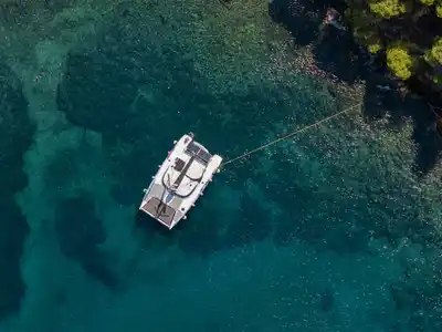Catamaran moored off a rocky pine shore in clear green water at Agia Kyriaki