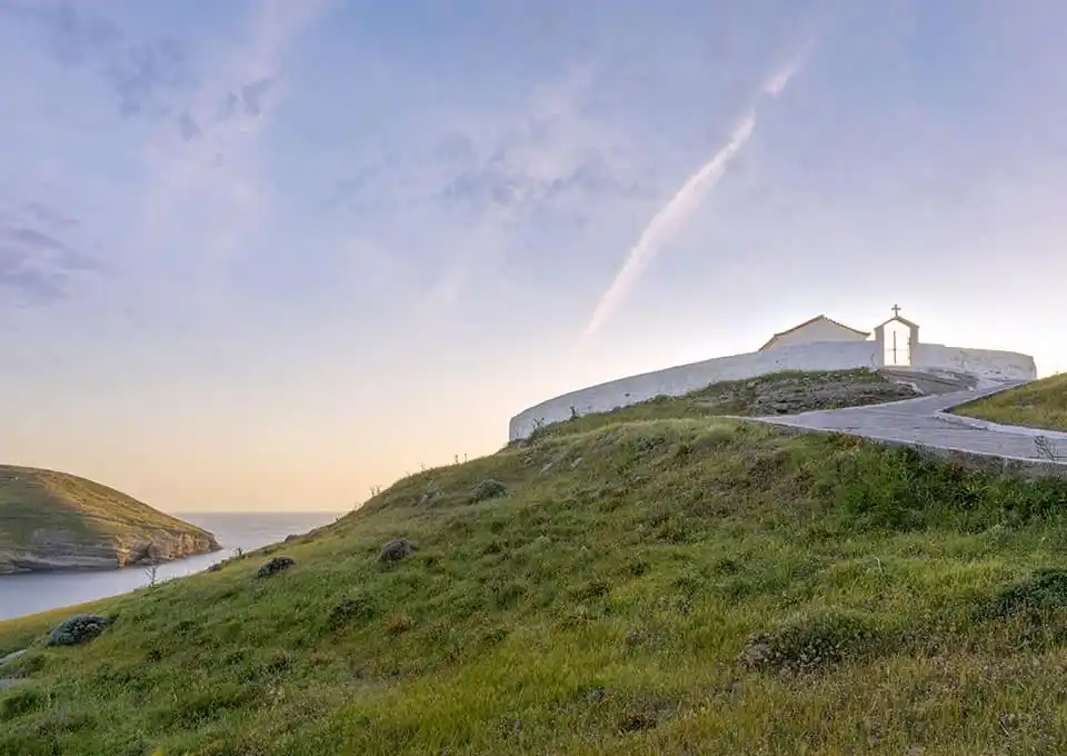 White chapel on a green hill above the sea at dusk