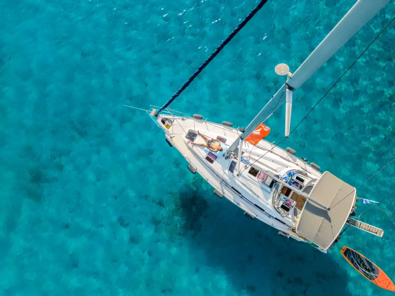 Το Bavaria 40 Babasails από ψηλά, πάνω από τιρκουάζ νερά στις Σποράδες, με μια επισκέπτρια να κάνει ηλιοθεραπεία στην πλώρη