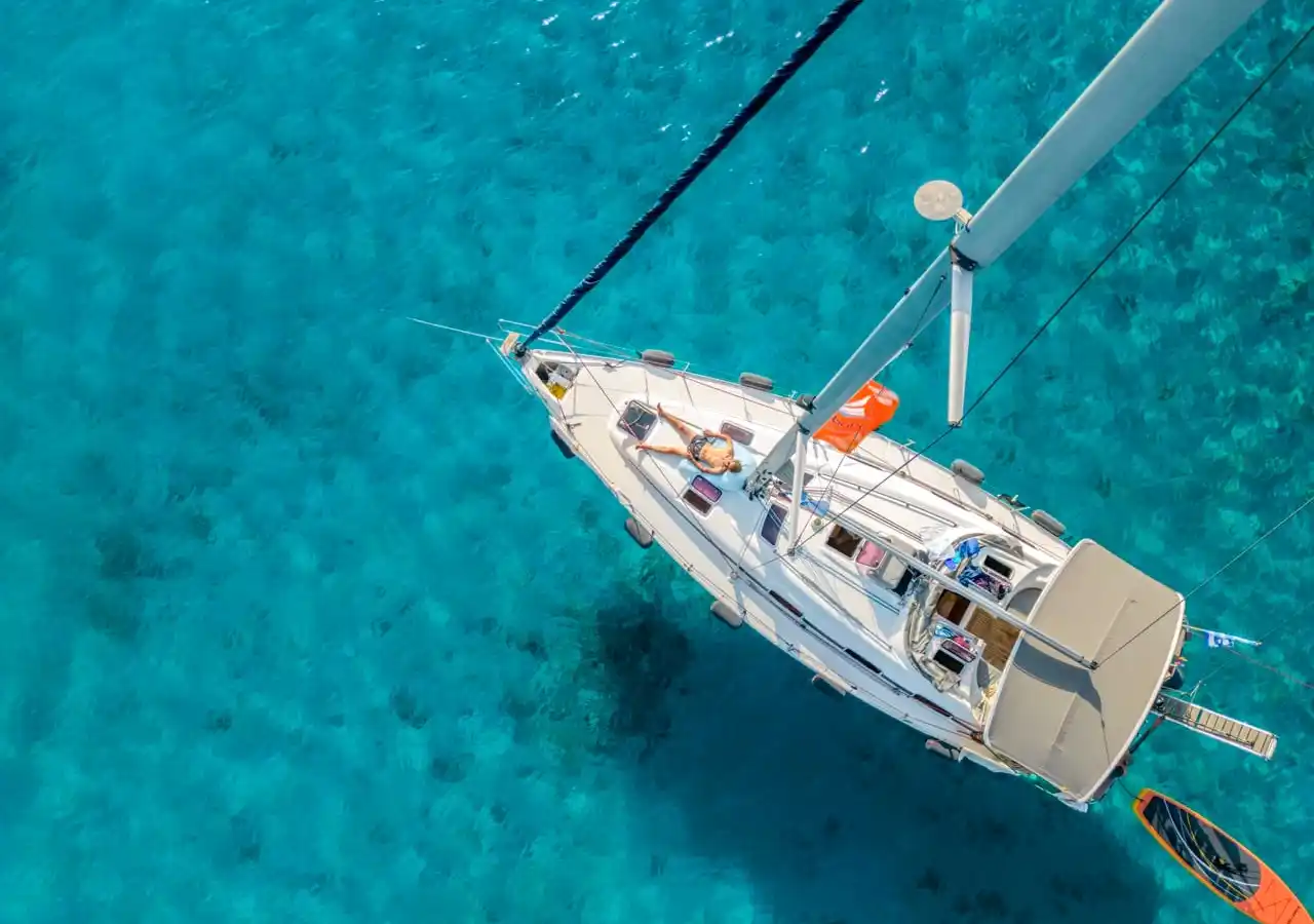 Το Bavaria 40 Babasails από ψηλά, πάνω από τιρκουάζ νερά στις Σποράδες, με μια επισκέπτρια να κάνει ηλιοθεραπεία στην πλώρη