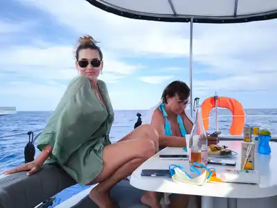 Two guests relaxing at a catamaran’s shaded cockpit table at sea