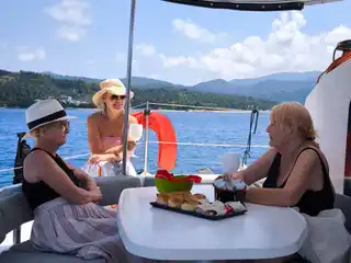 Three women sharing snacks at a catamaran’s shaded cockpit table