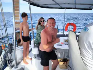 Family smiling in the shaded cockpit of a catamaran at sea