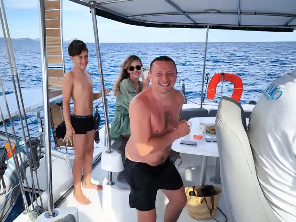 Family smiling in the shaded cockpit of a catamaran at sea