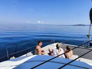 Friends on a catamaran’s bow on a calm open sea, an islet in the distance