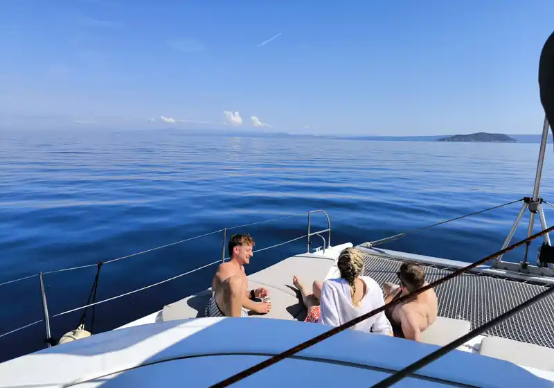 Friends on a catamaran’s bow on a calm open sea, an islet in the distance