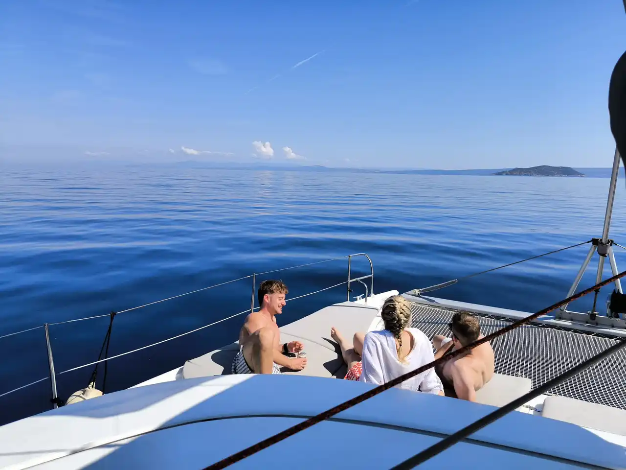 Friends on a catamaran’s bow on a calm open sea, an islet in the distance