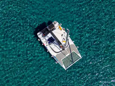 Catamaran anchored alone on rippled turquoise water, seen from directly above