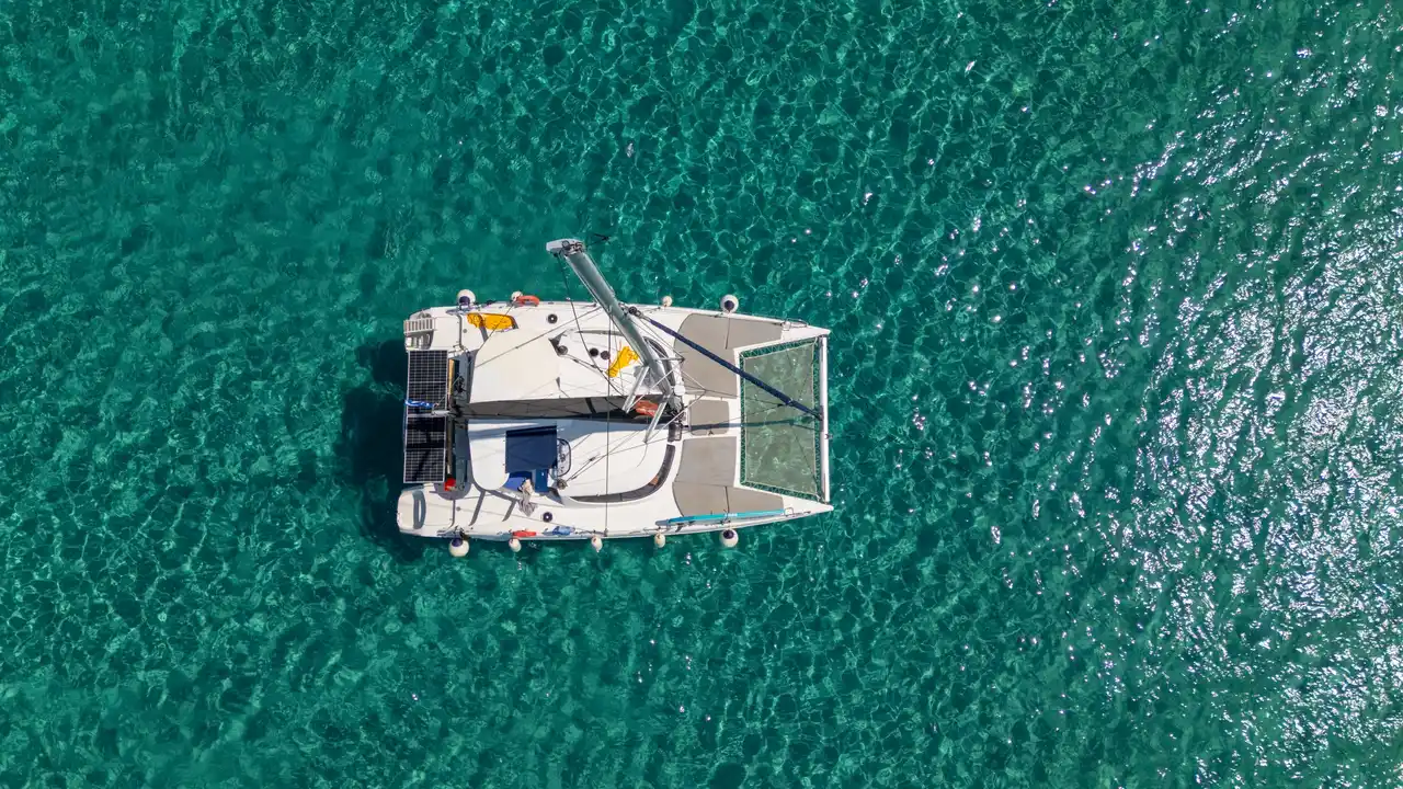 Το κατάστρωμα και τα δίχτυα ενός καταμαράν πάνω από τιρκουάζ νερά, από ψηλά