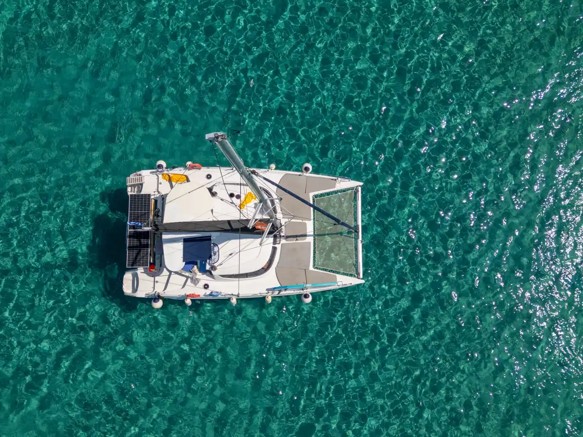 Το κατάστρωμα και τα δίχτυα ενός καταμαράν πάνω από τιρκουάζ νερά, από ψηλά
