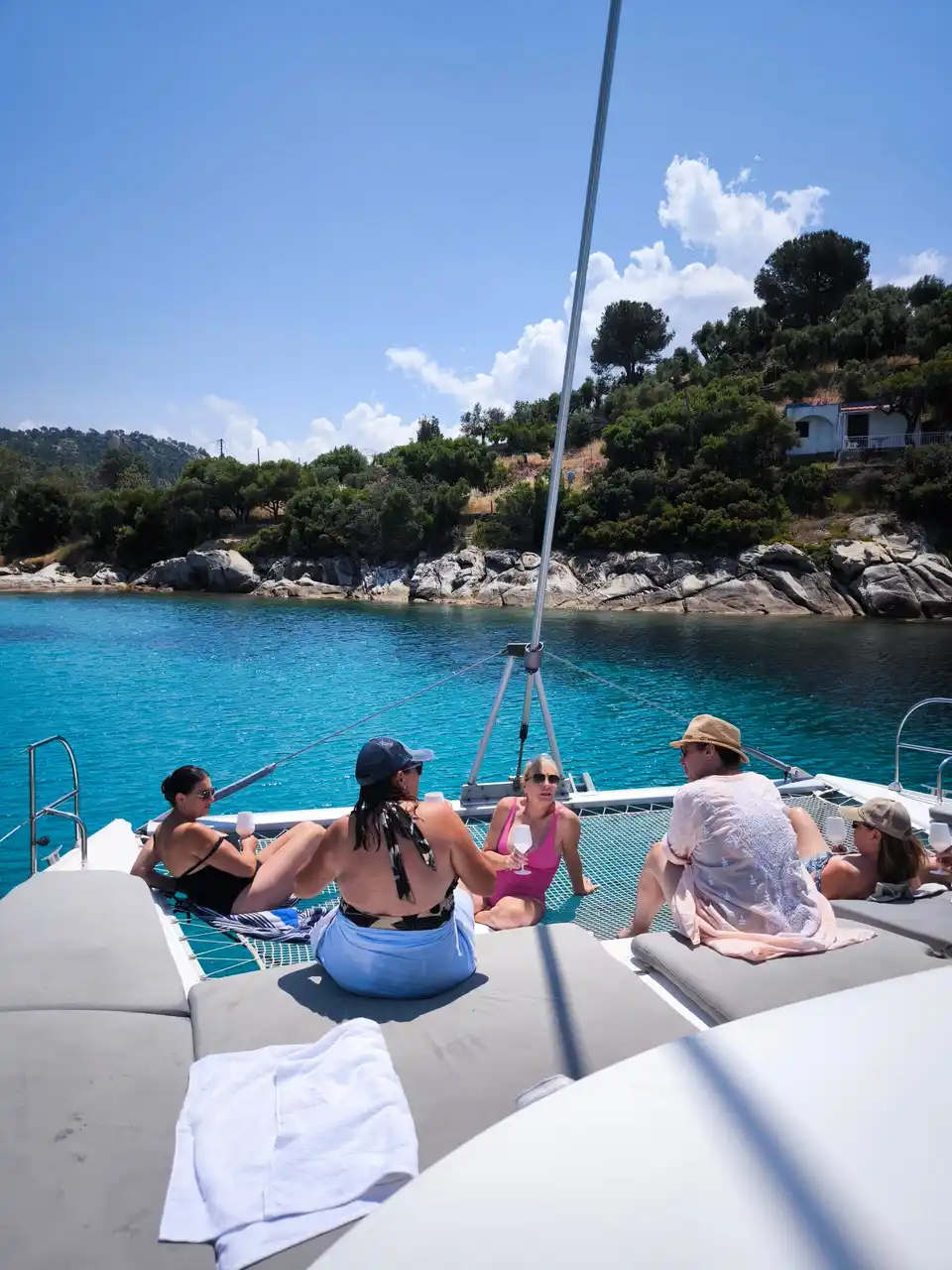 Guests relaxing on a catamaran’s bow nets in a turquoise cove