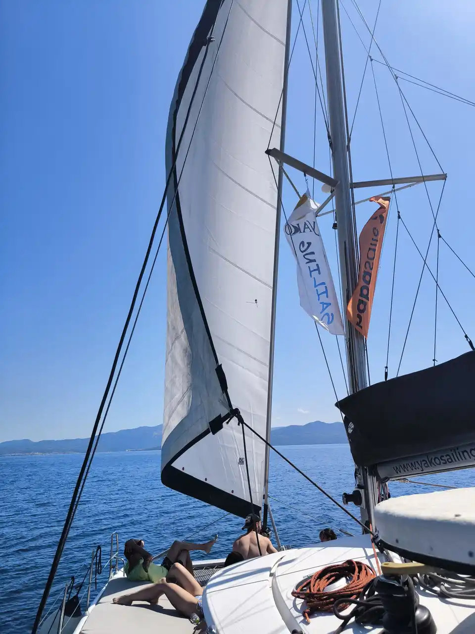 Guests lying on a catamaran’s bow as it sails under the genoa