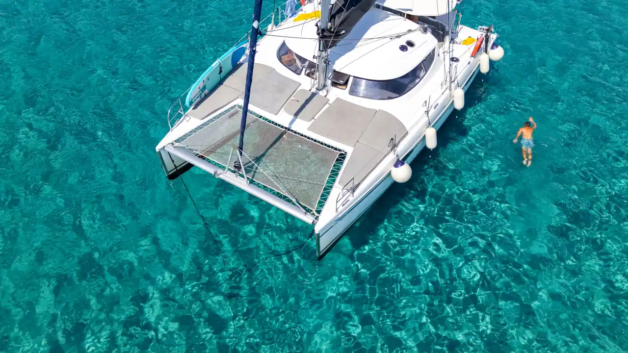 Καταμαράν στην άγκυρα σε καθαρά τιρκουάζ νερά, με κάποιον να κολυμπά δίπλα στη γάστρα