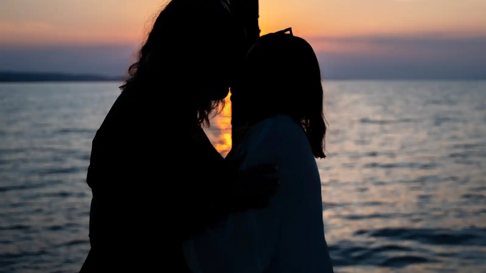 Silhouette of a couple embracing on a yacht as the sun sets over the sea