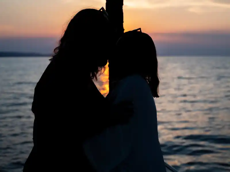 Silhouette of a couple embracing on a yacht as the sun sets over the sea