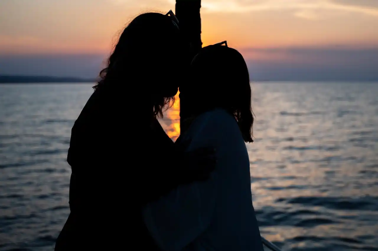Silhouette of a couple embracing on a yacht as the sun sets over the sea