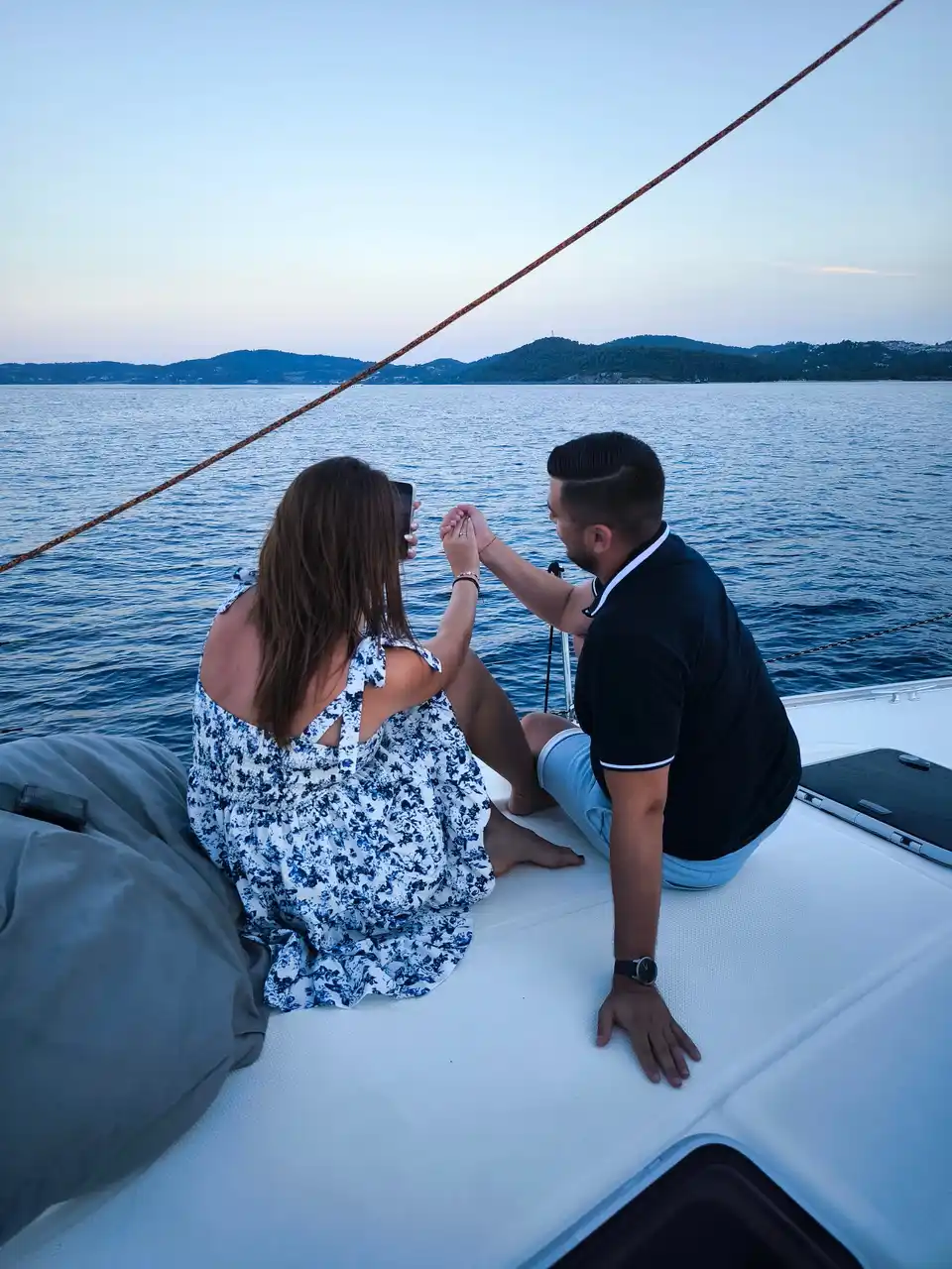 Couple sharing a toast on a sailing yacht’s bow at dusk