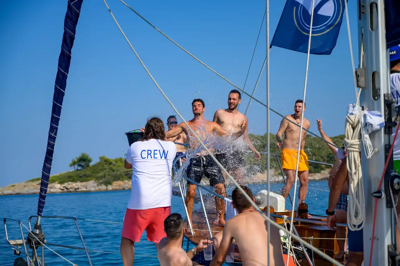Crew member splashing laughing guests with a bucket of water on a sailing yacht