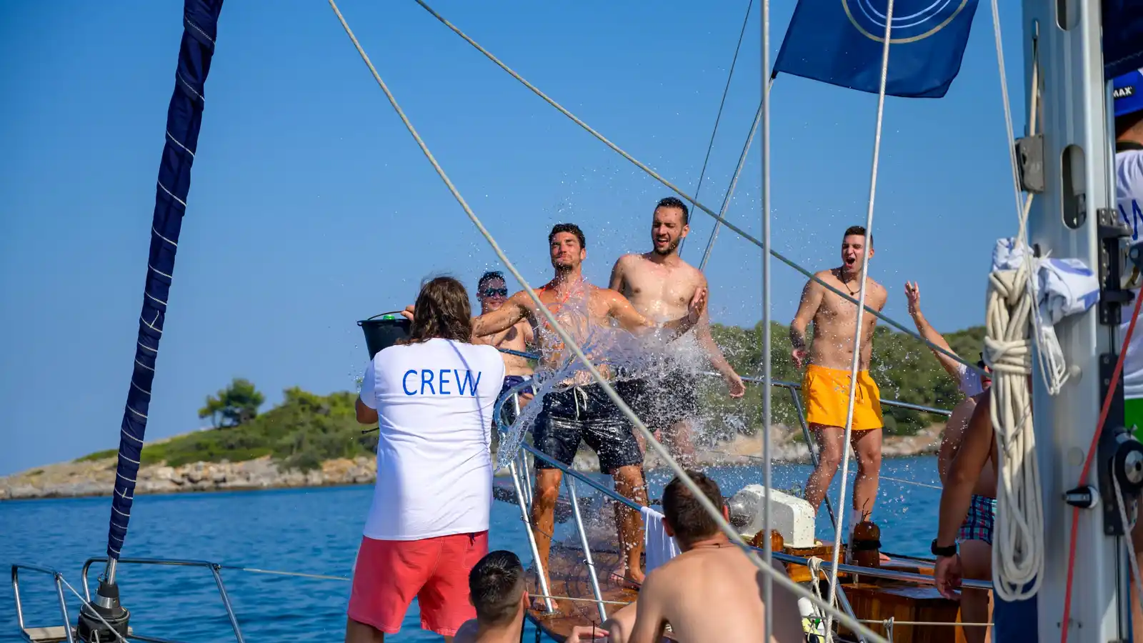 Crew member splashing laughing guests with a bucket of water on a sailing yacht