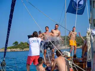 Crew member splashing laughing guests with a bucket of water on a sailing yacht