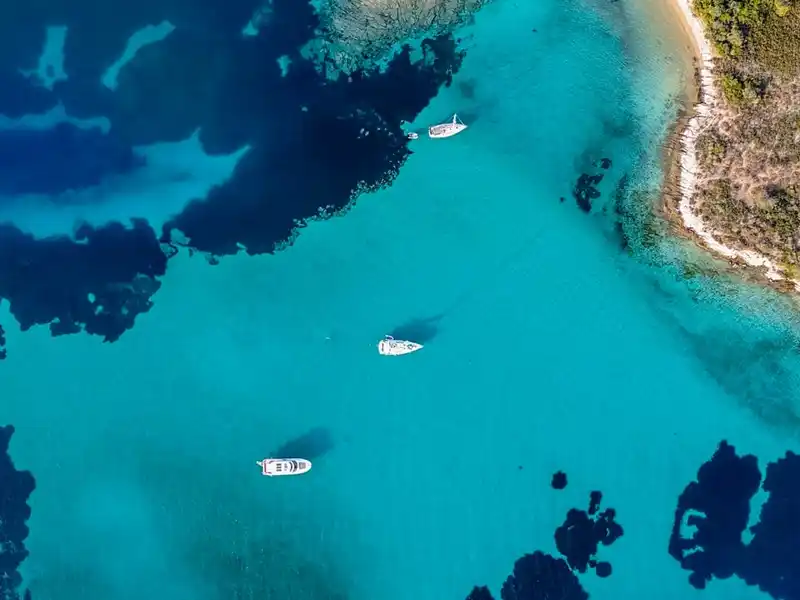 Three boats anchored over turquoise shallows off Diaporos