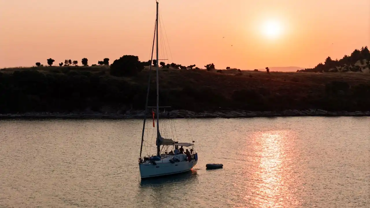 Sailing yacht anchored off Diaporos at sunset, a wooded island behind