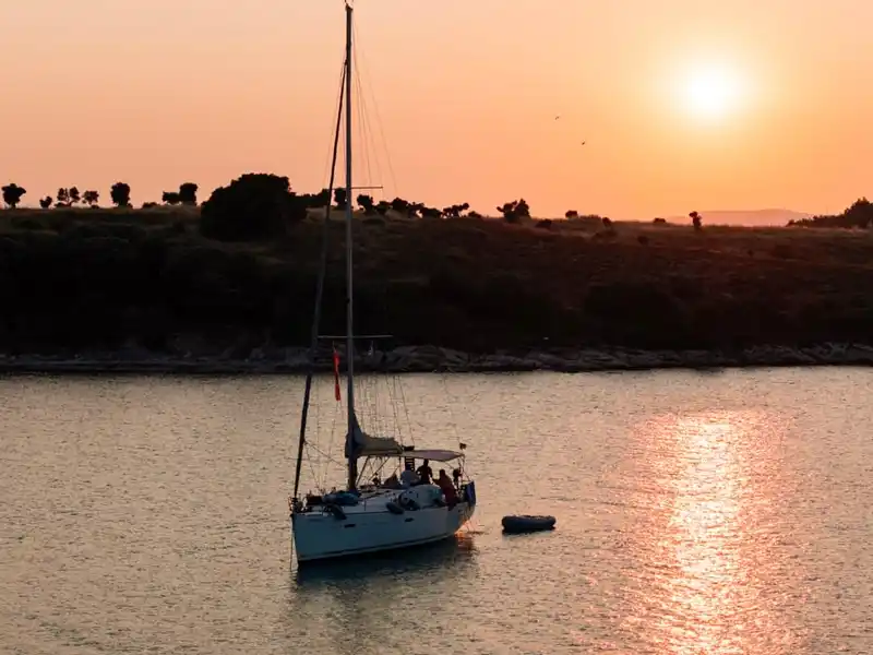 Sailing yacht anchored off Diaporos at sunset, a wooded island behind