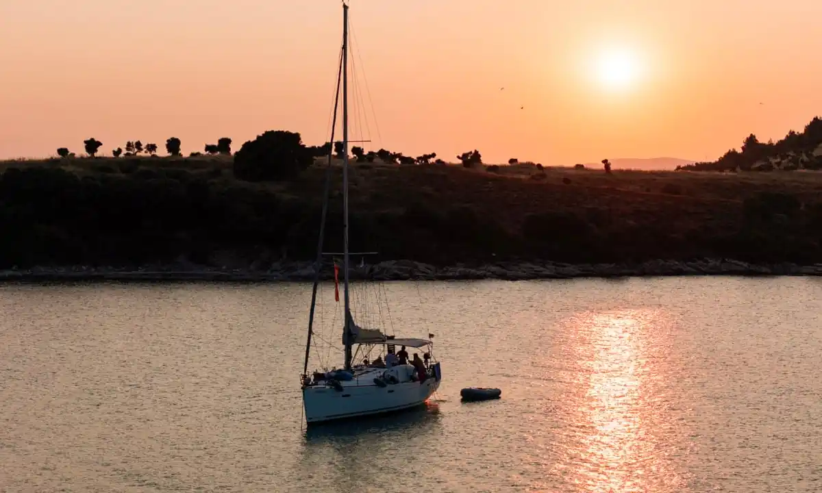 Sailing yacht anchored off Diaporos at sunset, a wooded island behind