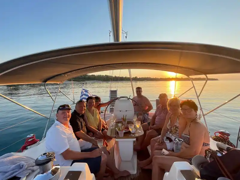 Group of friends smiling in a sailing yacht’s cockpit at sunset