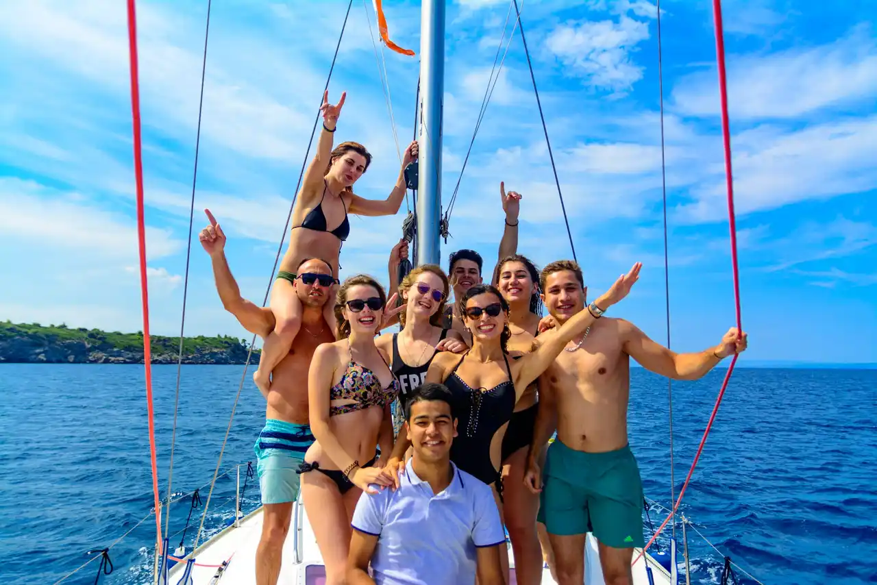 Group of friends posing and cheering on the bow of a sailing yacht