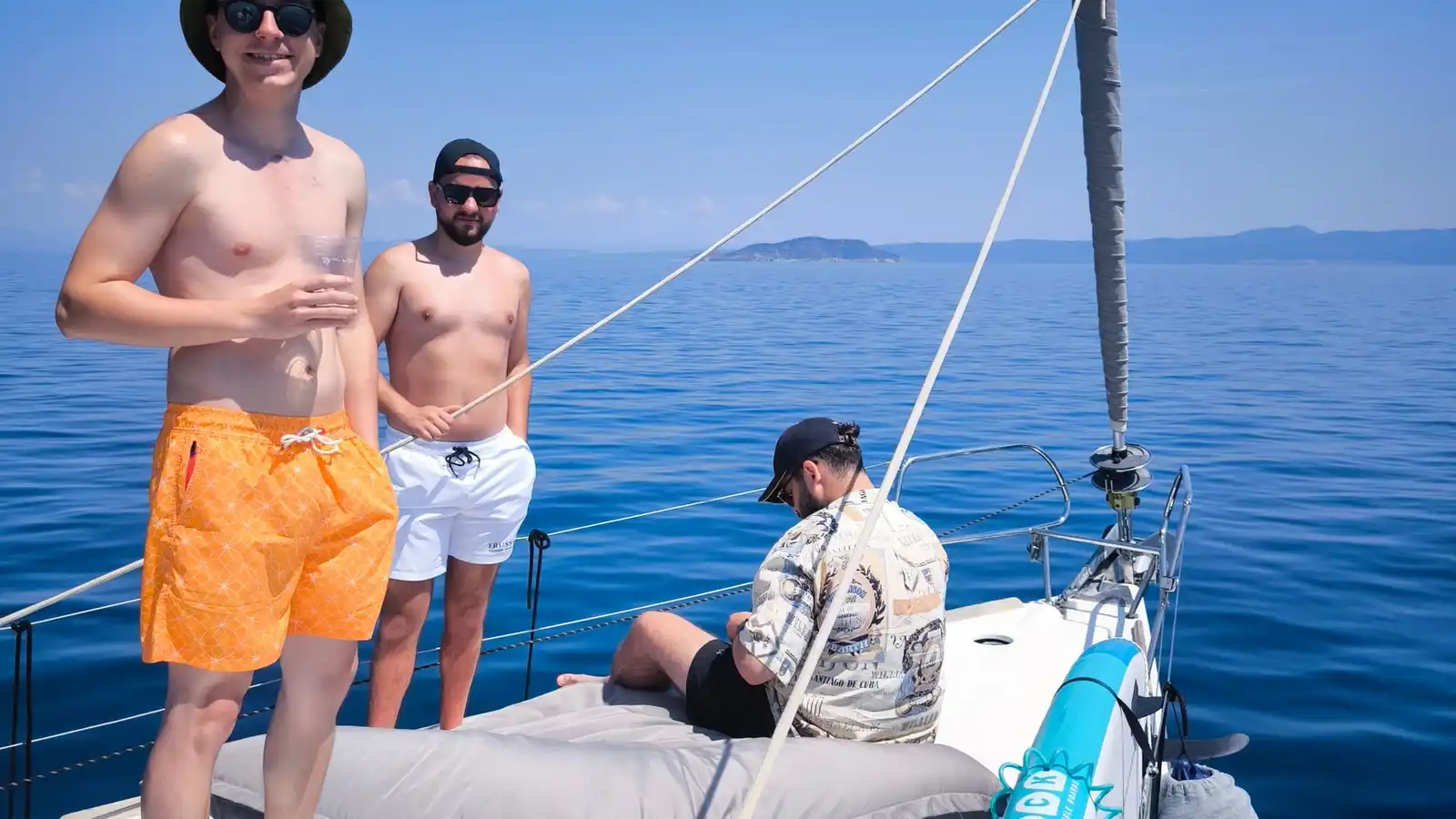 Friends standing on a sailing yacht’s bow on a calm blue sea