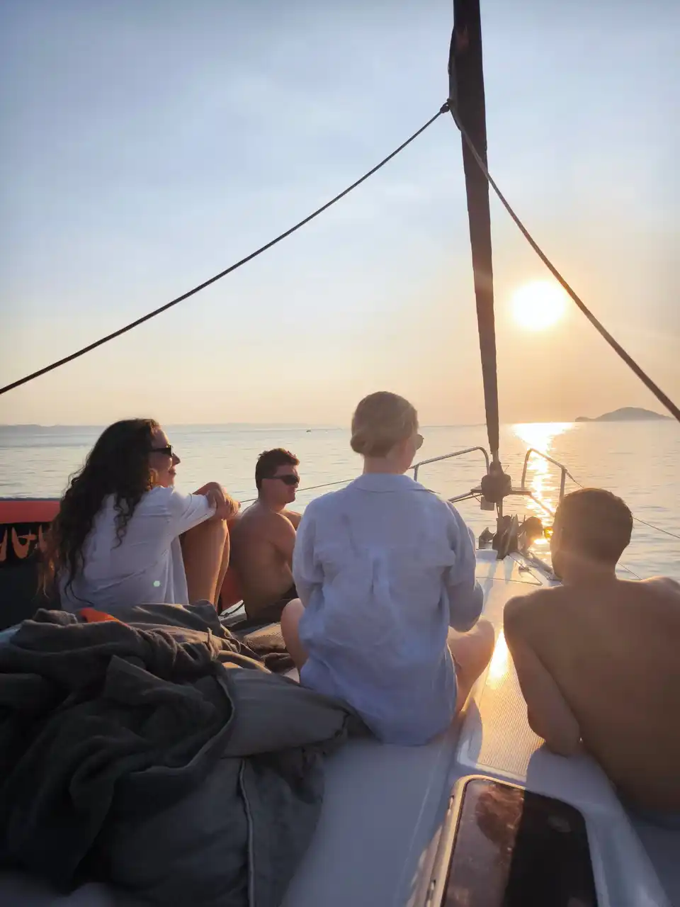 Friends sitting on a sailing yacht’s bow watching the sun set