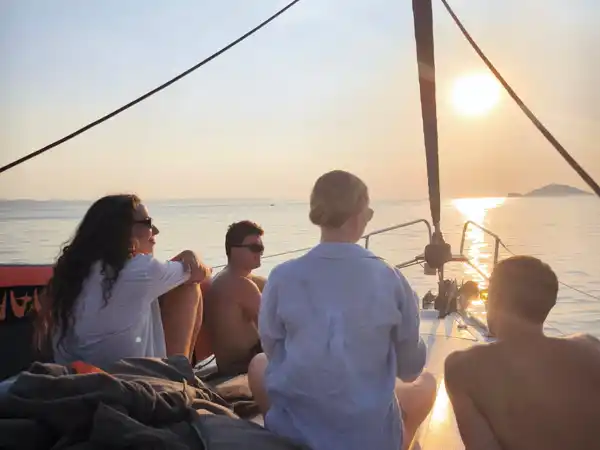 Friends sitting on a sailing yacht’s bow watching the sun set