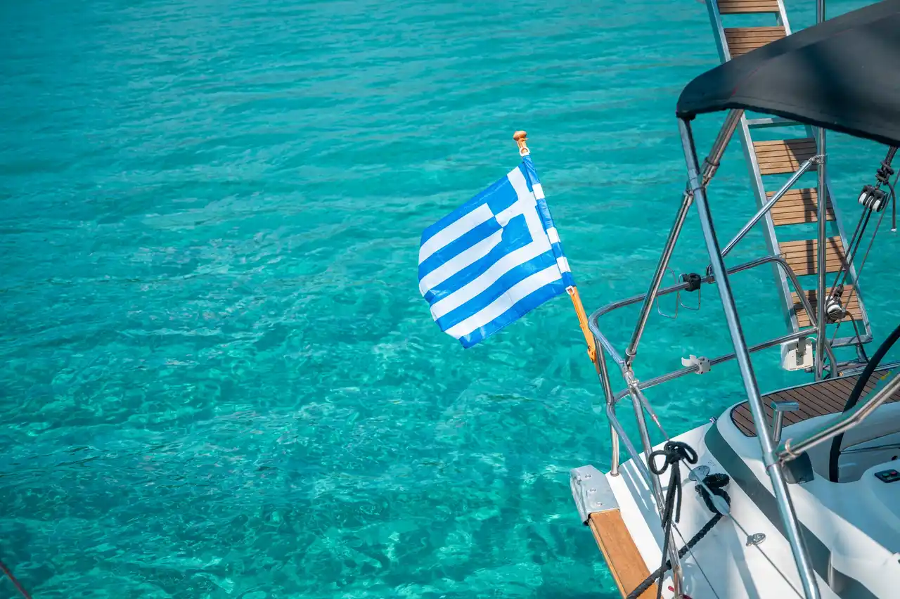Greek flag on the stern of a sailing yacht above turquoise water