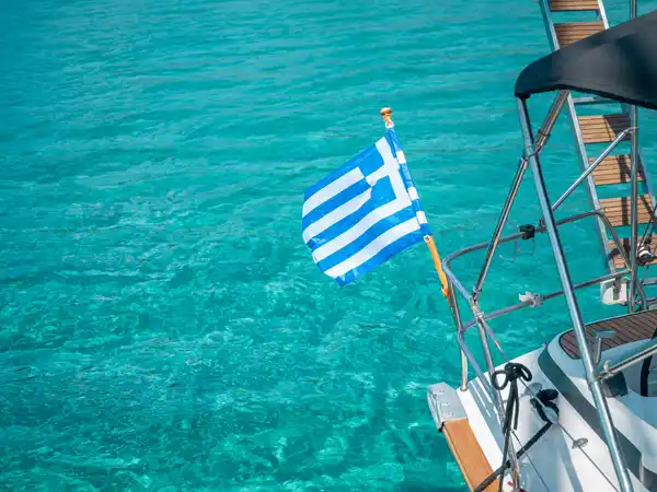 Greek flag on the stern of a sailing yacht above turquoise water