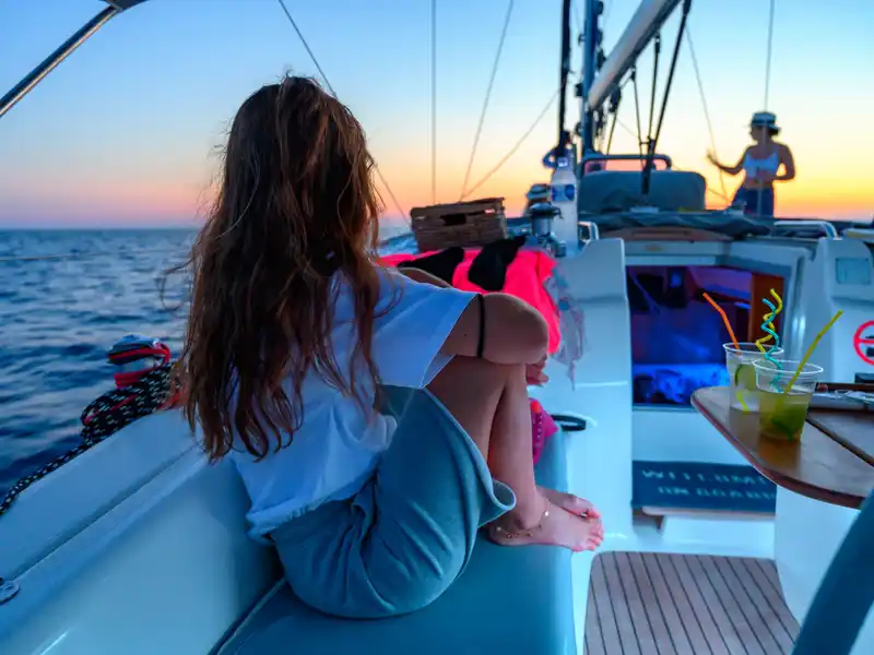Orange sky over guests on the deck of a sailing yacht at sunset