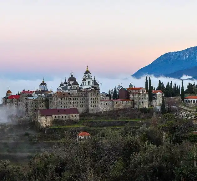 Large monastery with domes and towers in the morning mist, a mountain behind