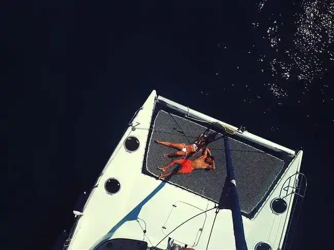 Two people sunbathing on the trampoline of a catamaran, seen from above