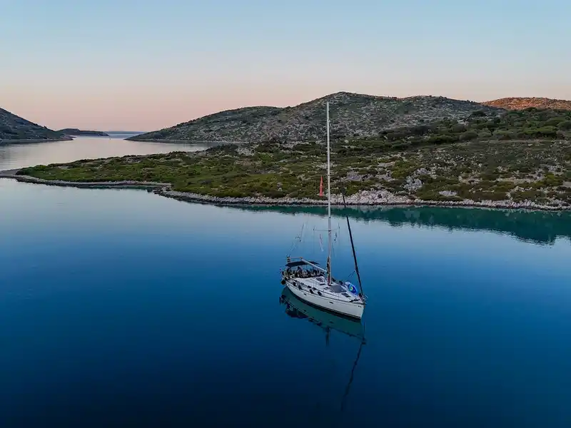 Sailing yacht at anchor on still water between low islands at dusk