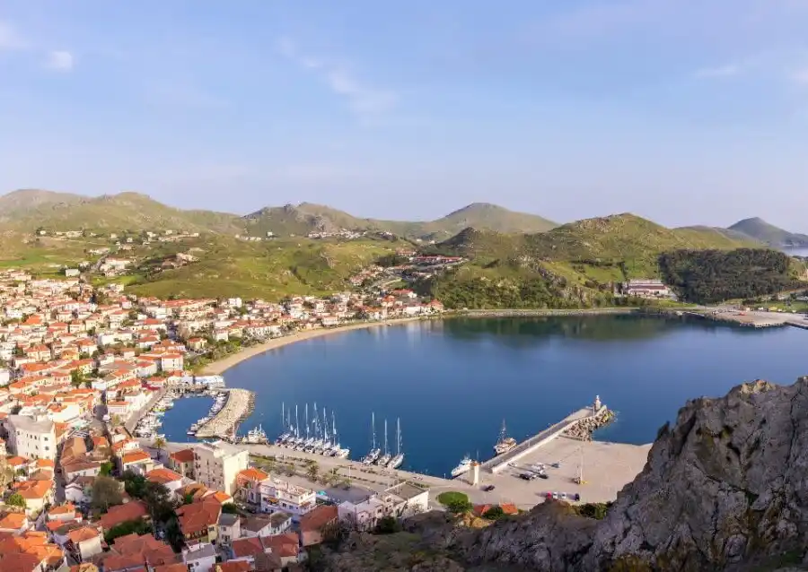 Town with red roofs around a harbour with sailing yachts, green hills behind