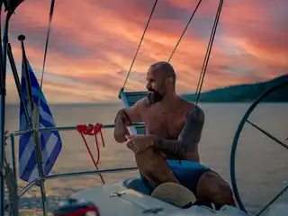 Man sitting at a sailing yacht’s helm under a red evening sky