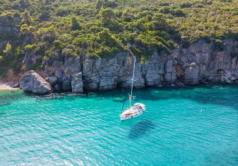 Ιστιοπλοϊκό σε τιρκουάζ νερά κάτω από γκρίζους ασβεστολιθικούς βράχους, στο Παλιούρι