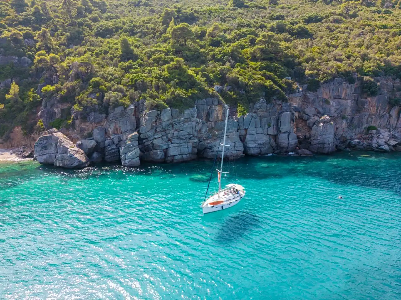 Sailing yacht anchored in turquoise water below grey limestone cliffs off Paliouri