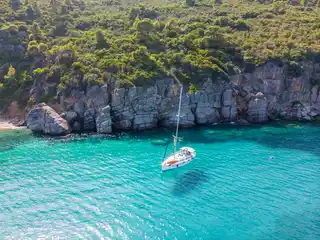 Sailing yacht anchored in turquoise water below grey limestone cliffs off Paliouri
