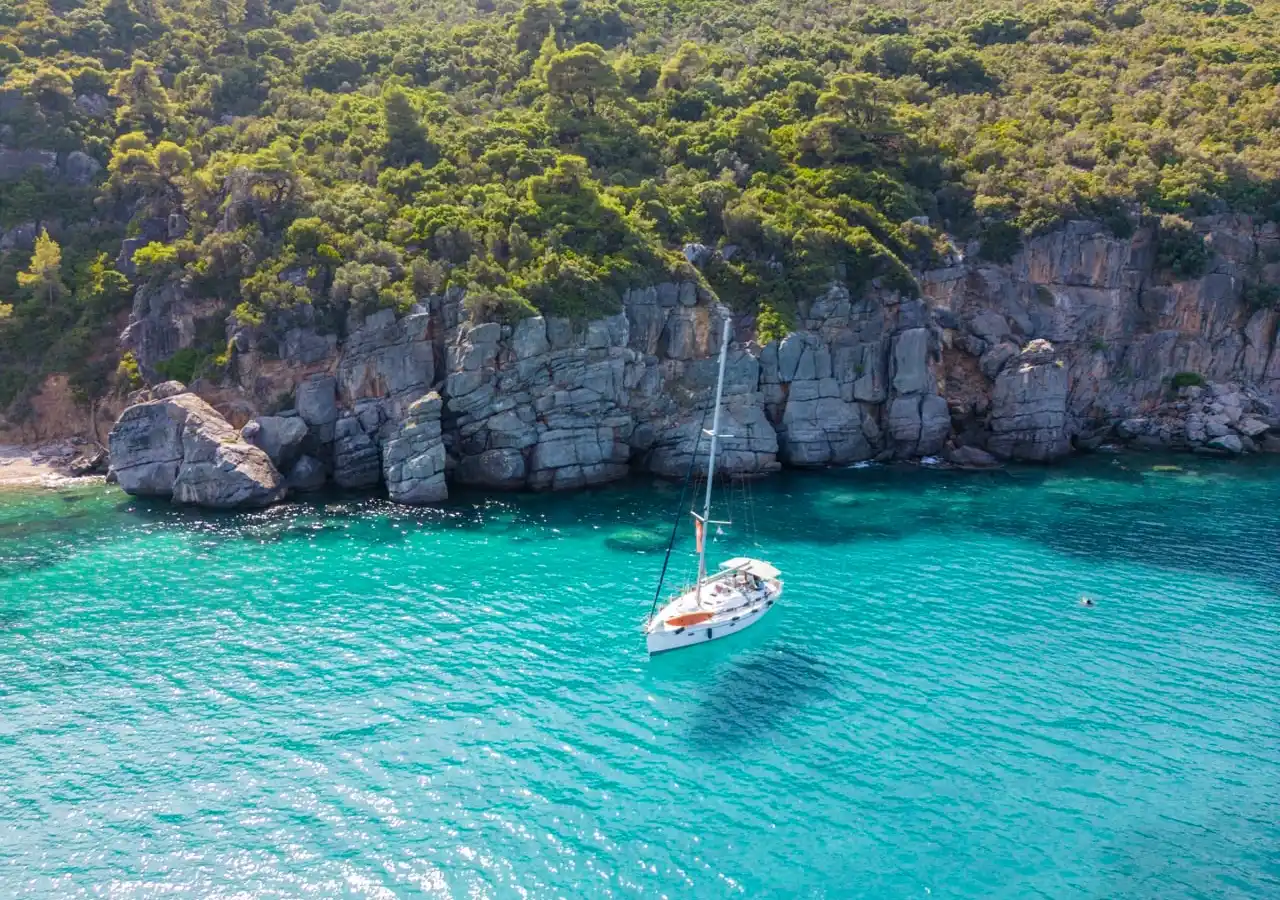 Sailing yacht anchored in turquoise water below grey limestone cliffs off Paliouri