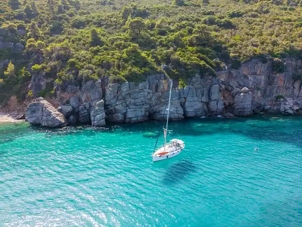 Sailing yacht anchored in turquoise water below grey limestone cliffs off Paliouri