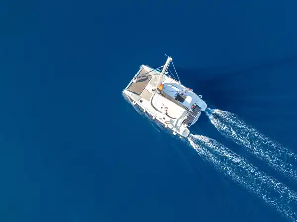 Catamaran leaving a white wake across deep blue water, seen from above